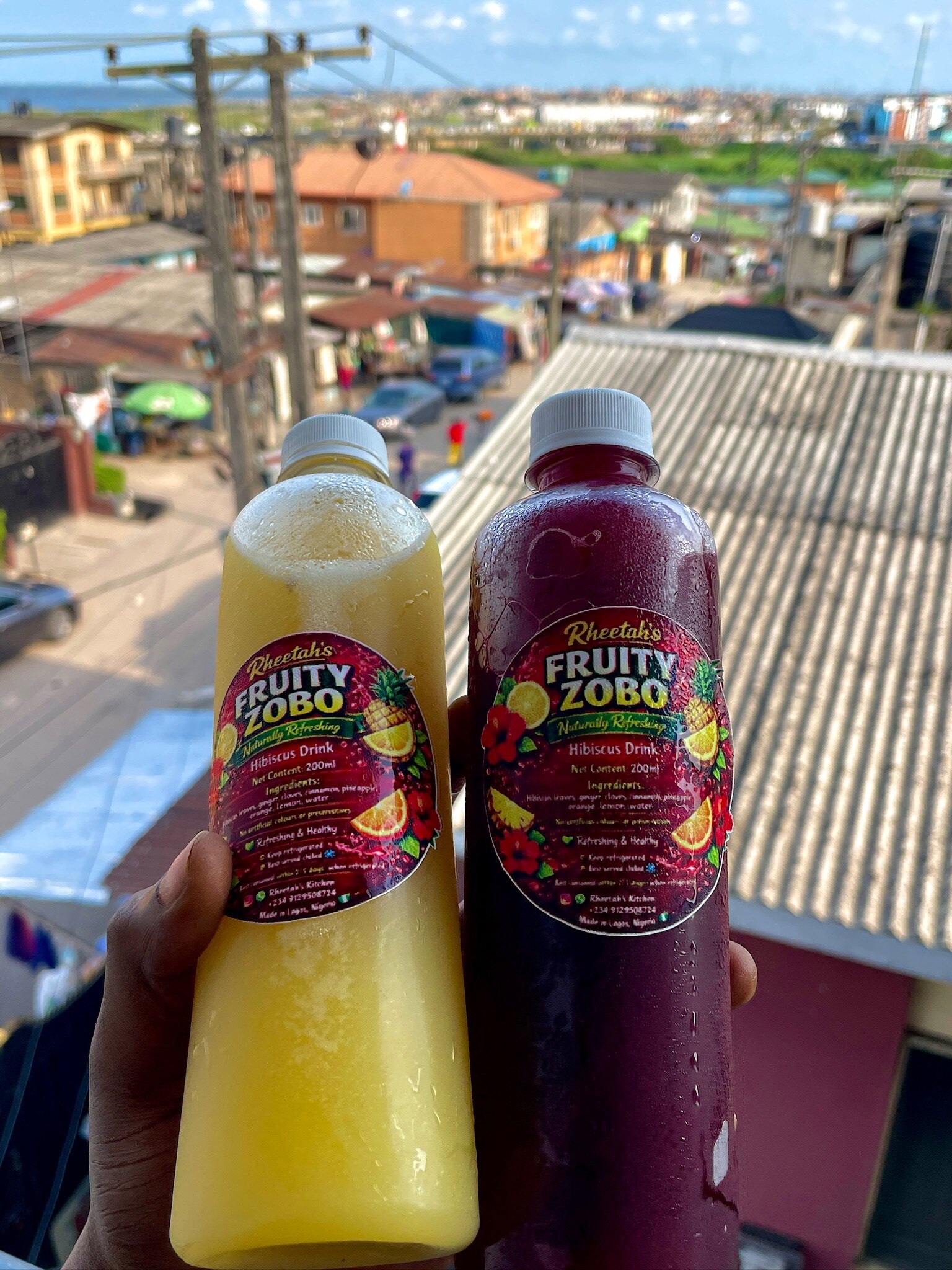 Two bottles of Rheetah's Fruity Zobo held up on a Lagos rooftop